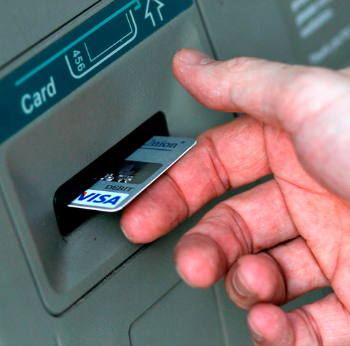 Hand inserting a card into an ATM slot.