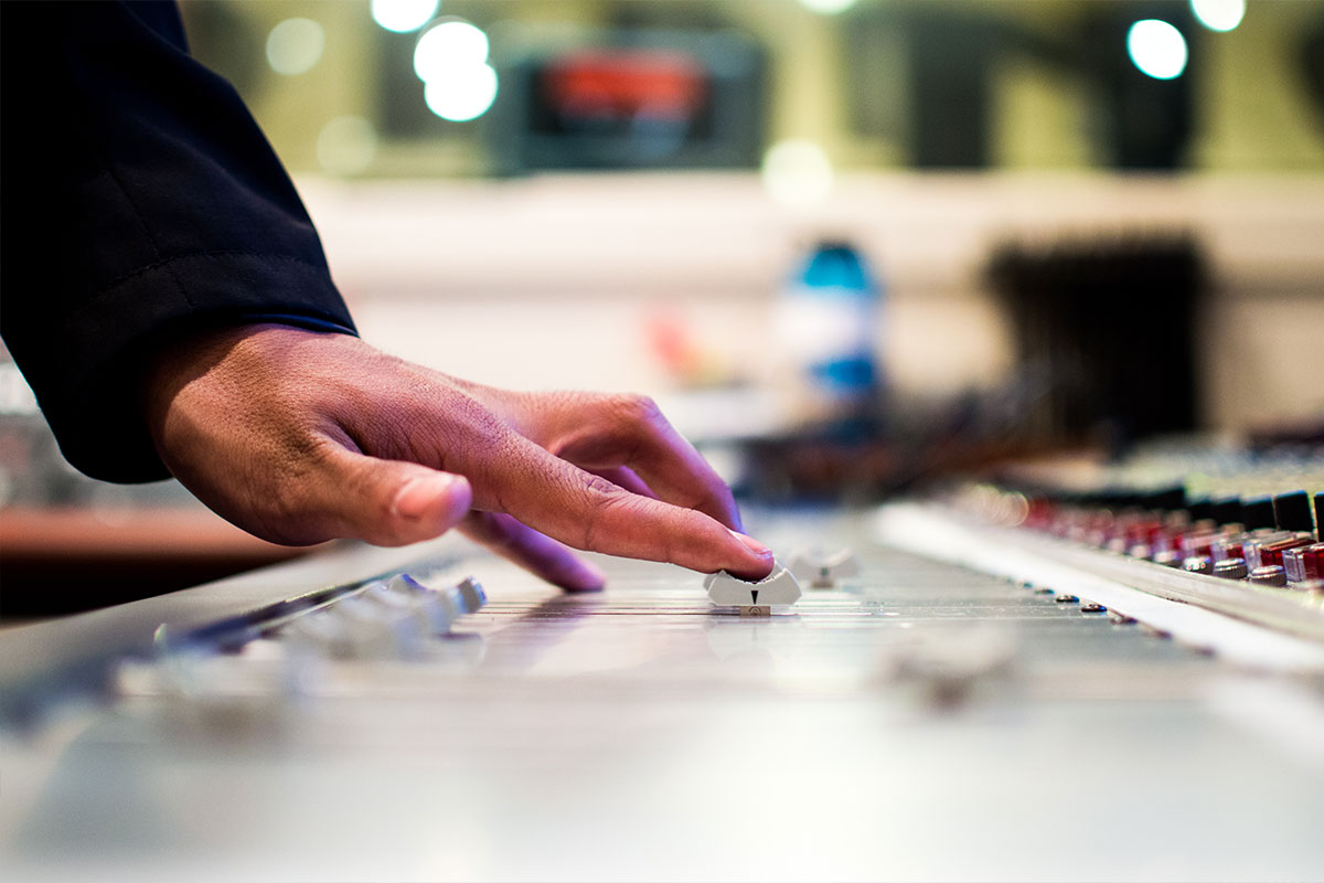 Hands adjusting controls on an audio mixer.